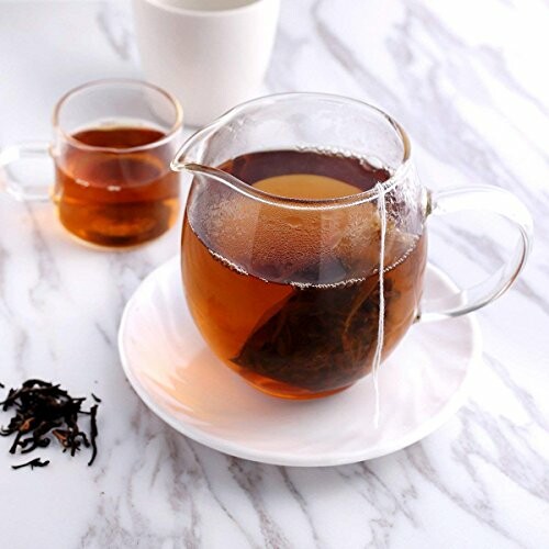 Glass teapot with tea bag and cup on marble table.